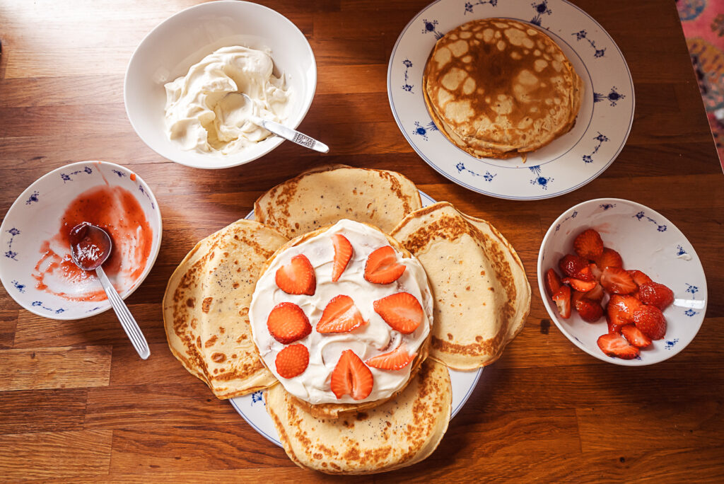 assembling Swedish pancake cake with cream and strawberry slices