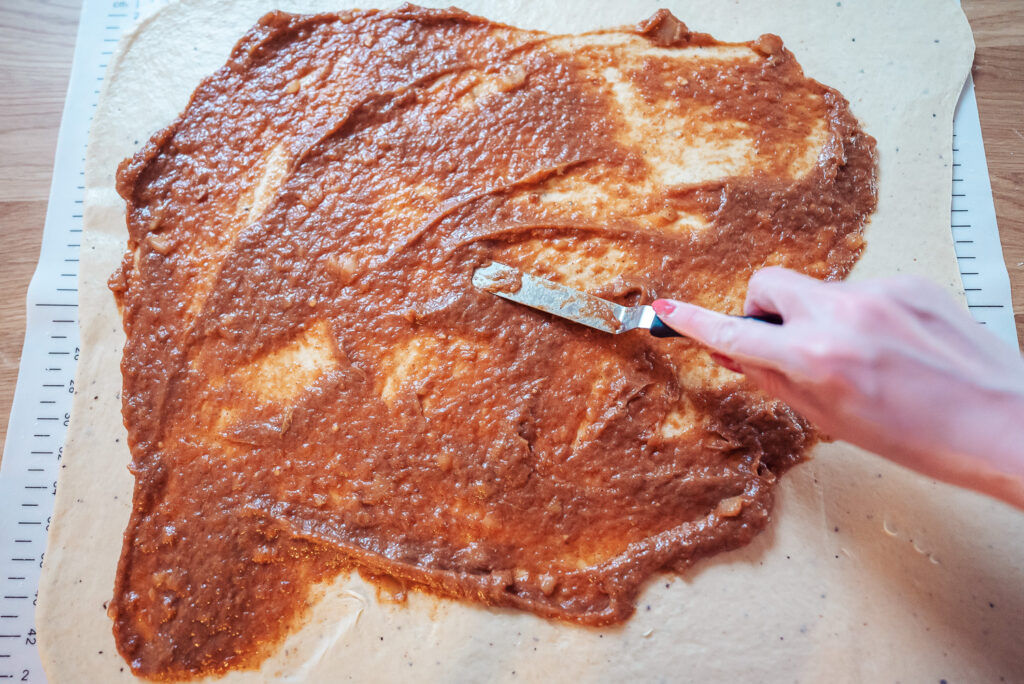 spreading apple sauce filling across cinnamon bun dough