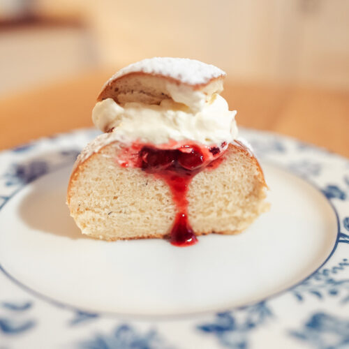 Norwegian fastelavnsboller with jam and whipped cream sliced in half on a plate